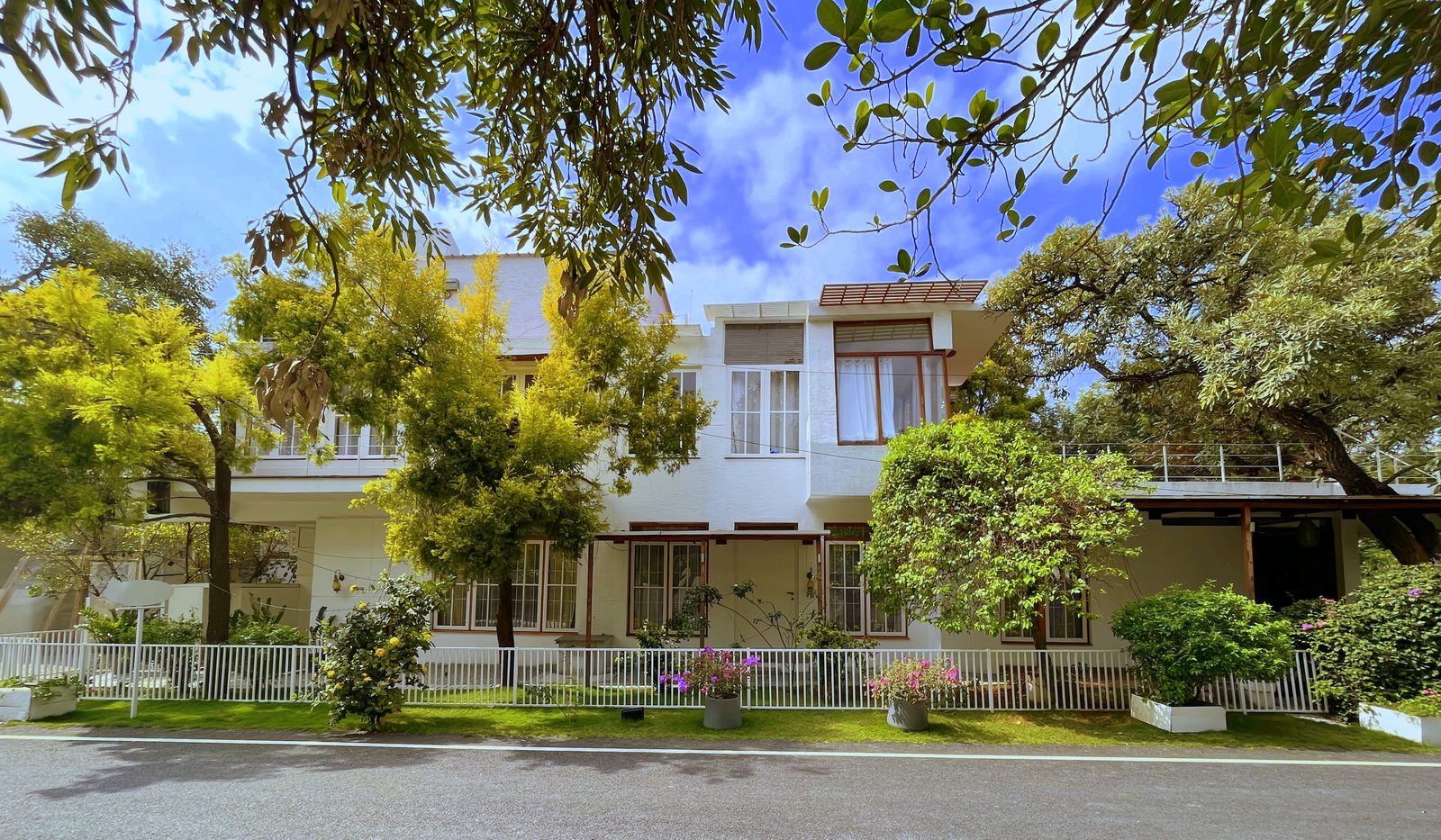 TA House — long road frontage seen from the street behind a white picket fence
