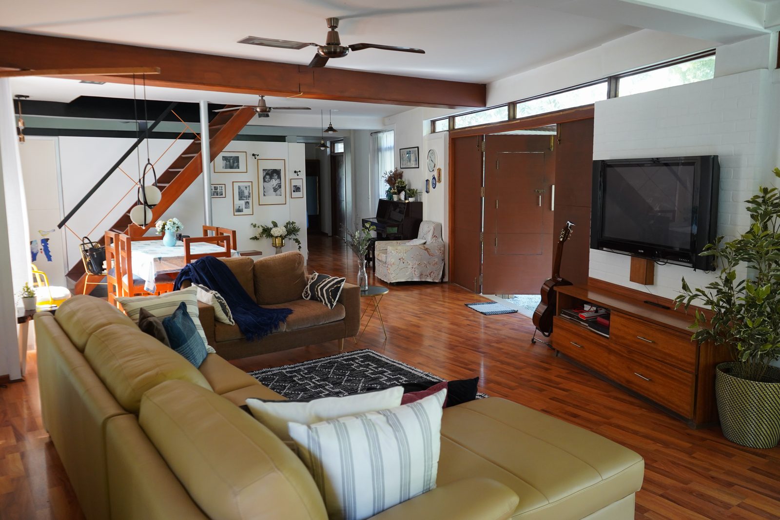 TA House — open-plan living room with leather sofas, gallery wall and timber staircase