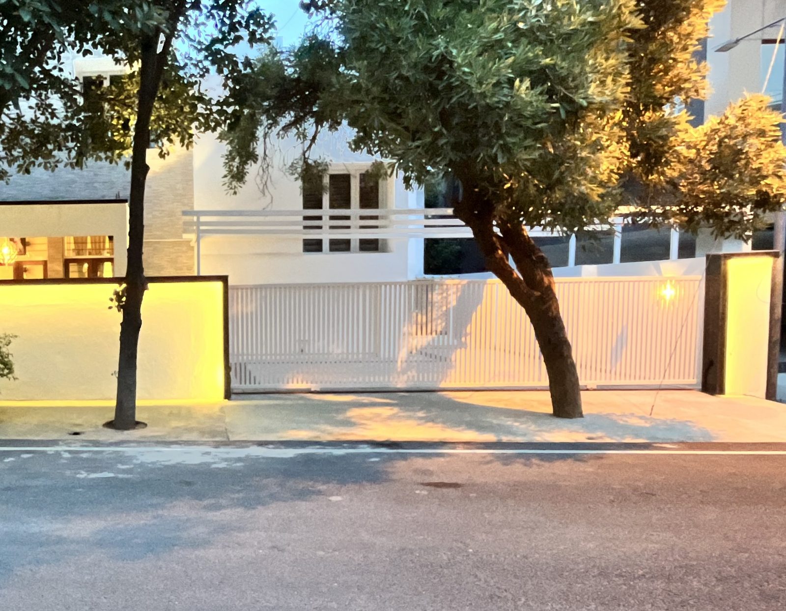 Gilbert — white street elevation behind a slatted gate at dusk