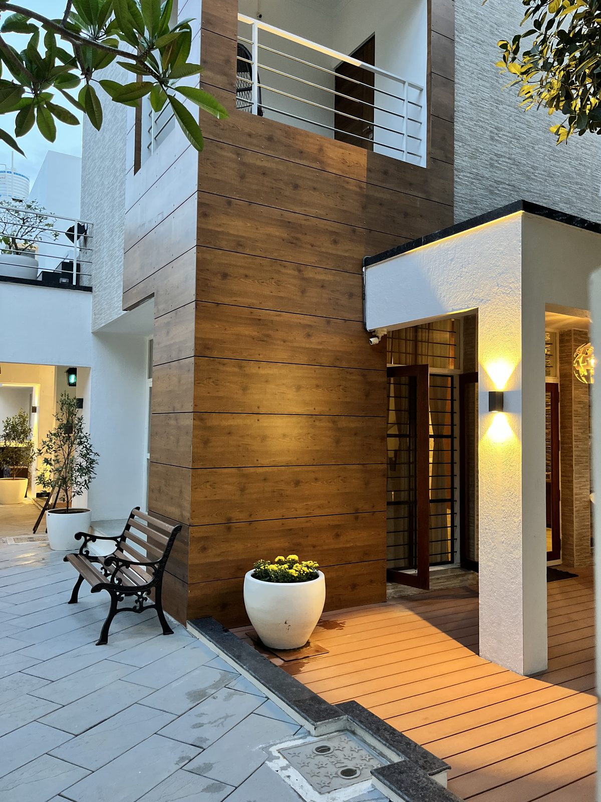 Gilbert — entry court with timber-clad wall, cast-iron bench and uplit doorway